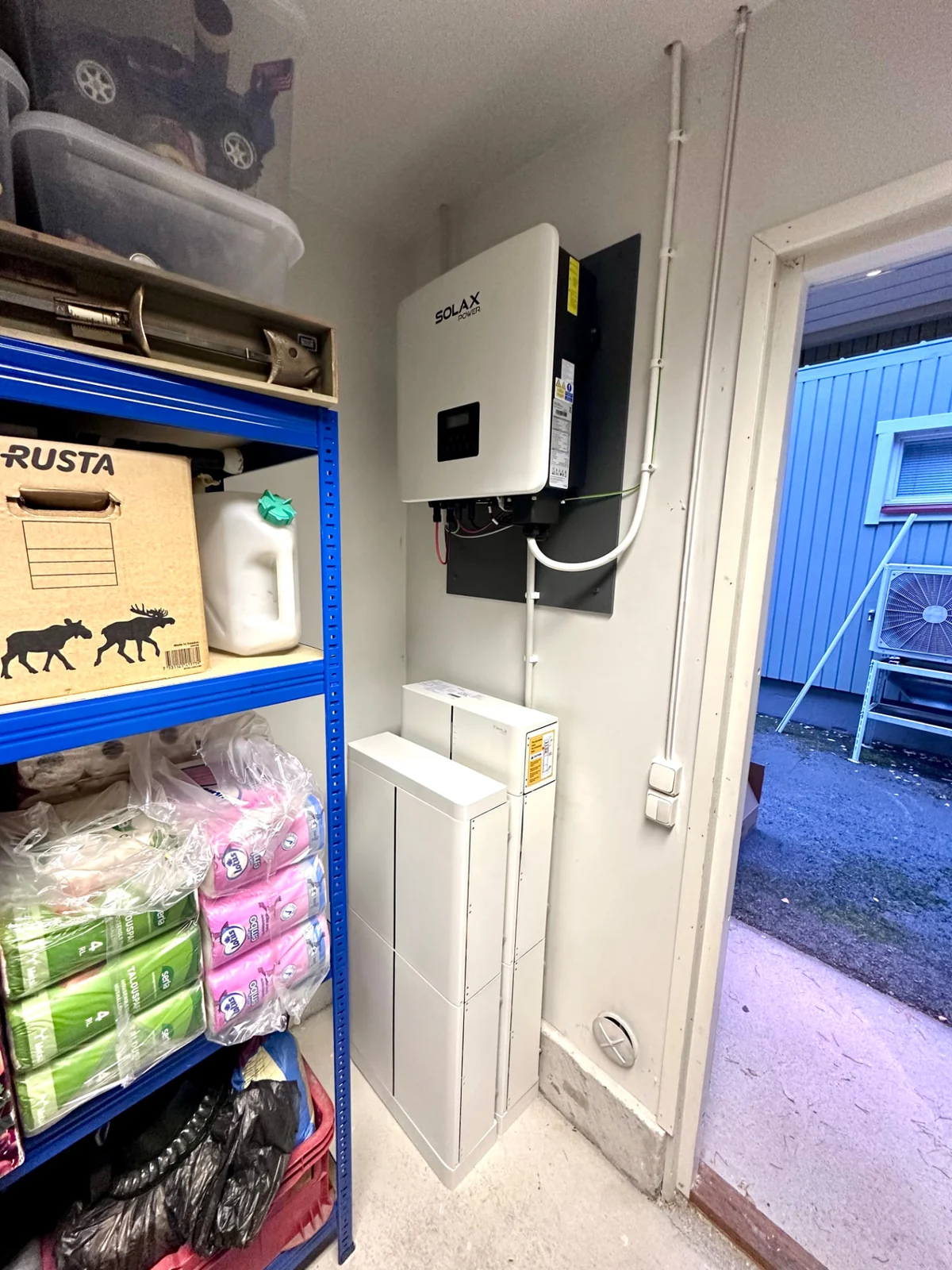 SolaX X3 Hybrid -invertteri seinällä ja 12,3&nbsp;kWh SolaX-akusto sen alapuolella omakotitalon varastotilassa